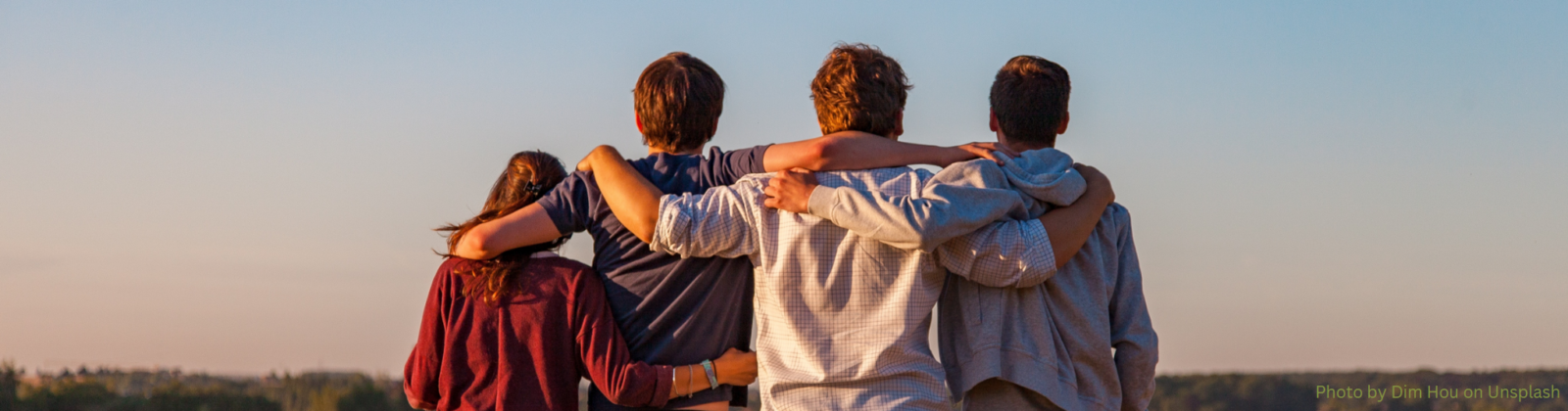 Four friends linking arms, overlooking a field.