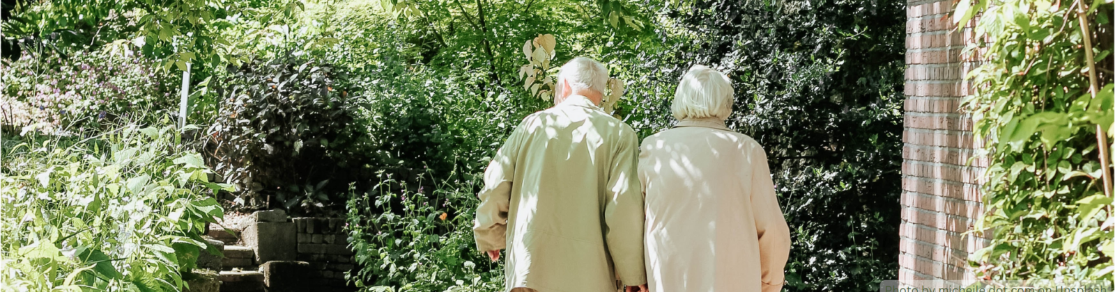 Elderly couple walking on a paved garden path.